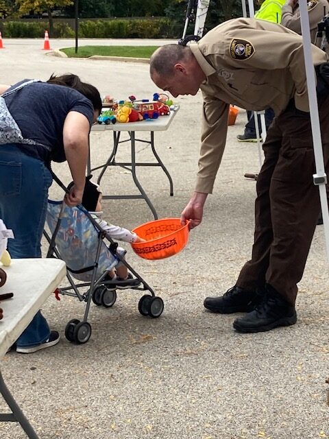 Sheriff's Police Officer giving candy to a child from a bowl at the Trunk or Treat event