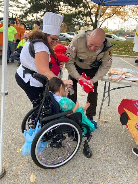 Sheriff's Police Officer leaning over speaking to a child in a wheelchair at the Trunk or Treat event