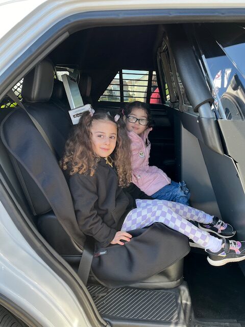 Young children sitting in the back of a Sheriff's Office squad car at the Touch a Truck event in Maine Township