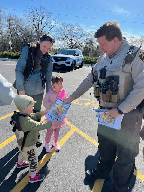 Sheriff's Police Officer handing a small book to a young child at the Touch a Truck event in Maine Township