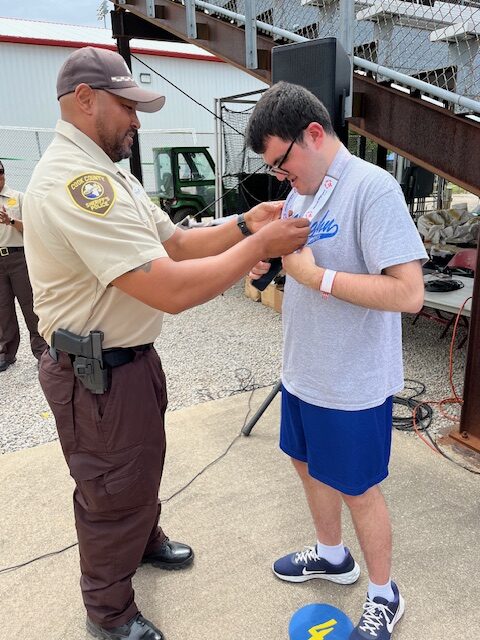 Member of the Sheriff's Office placing a medal on the neck of a participant at the Special Olympics Ceremony