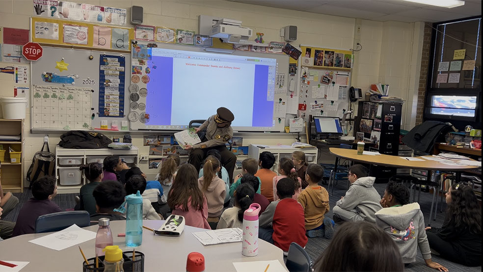 Sheriff's Police Officer sitting and showing the pages of a book to a group of young individuals at the Read Across America event in Glenview