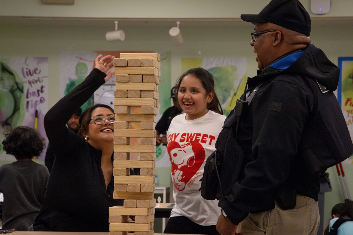 Sheriff's Police Officer playing a block tower game with two young individuals at the Haines Game Night