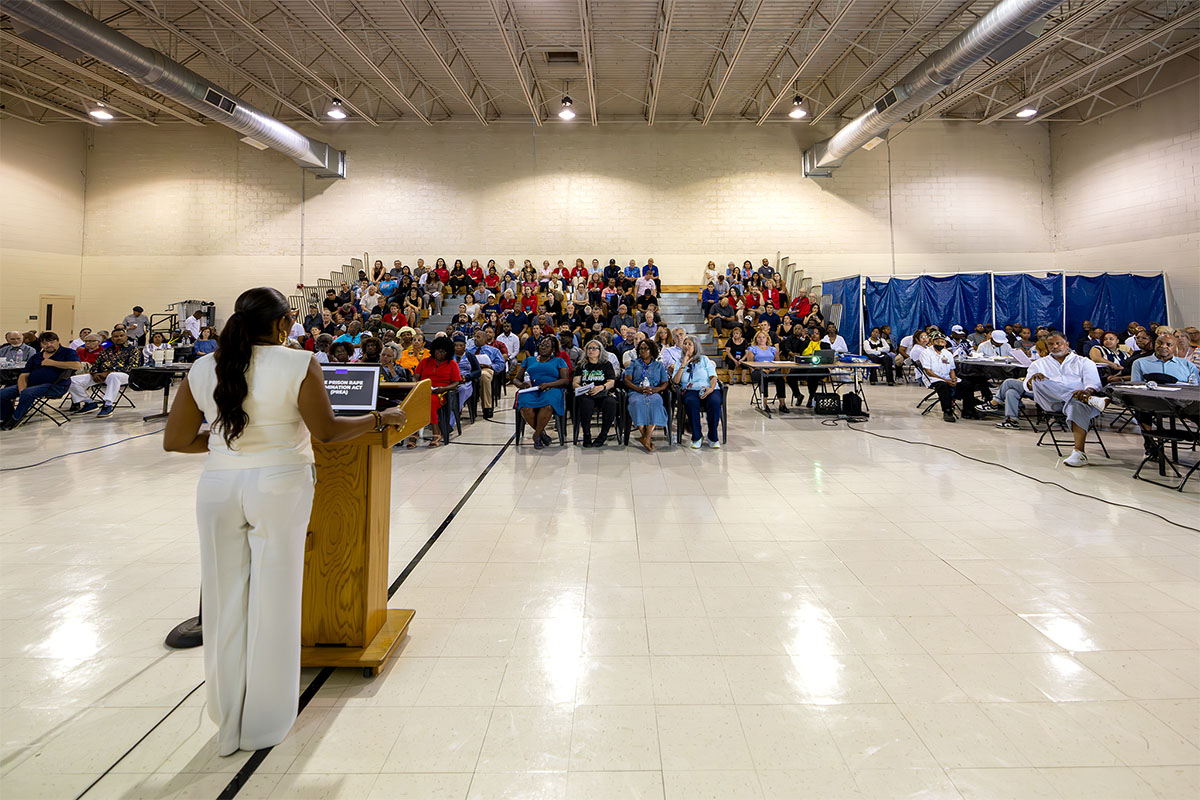 A person stands at a podium addressing a large audience seated in a spacious indoor venue.