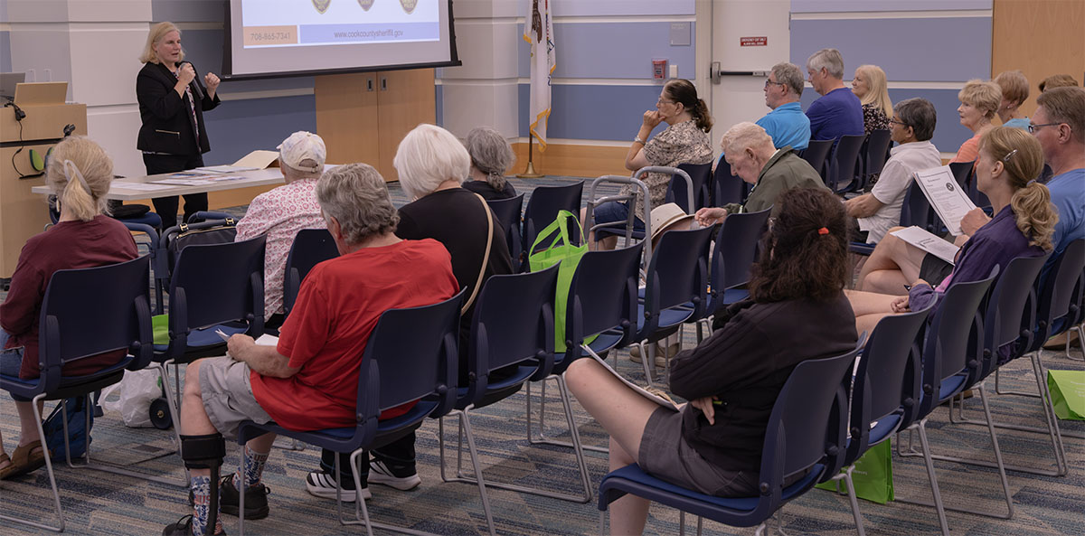 A speaker addresses an audience seated in rows of chairs during a presentation in a conference room.